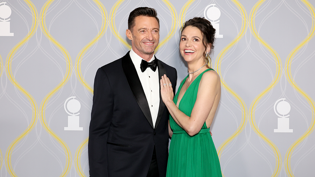 Hugh Jackman and Sutton Foster posing together at an event with a patterned backdrop, dressed formally.