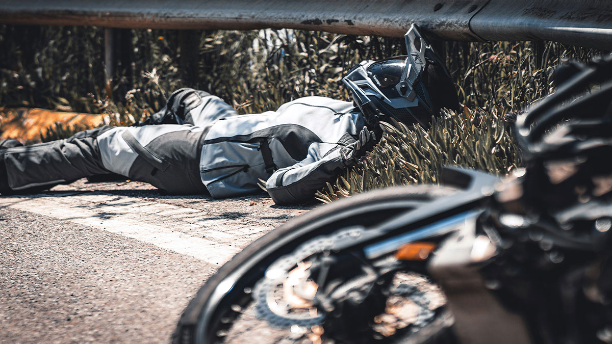 Motorcyclist in full gear lies injured by roadside after crash, highlighting tragedy in affair partner accident.
