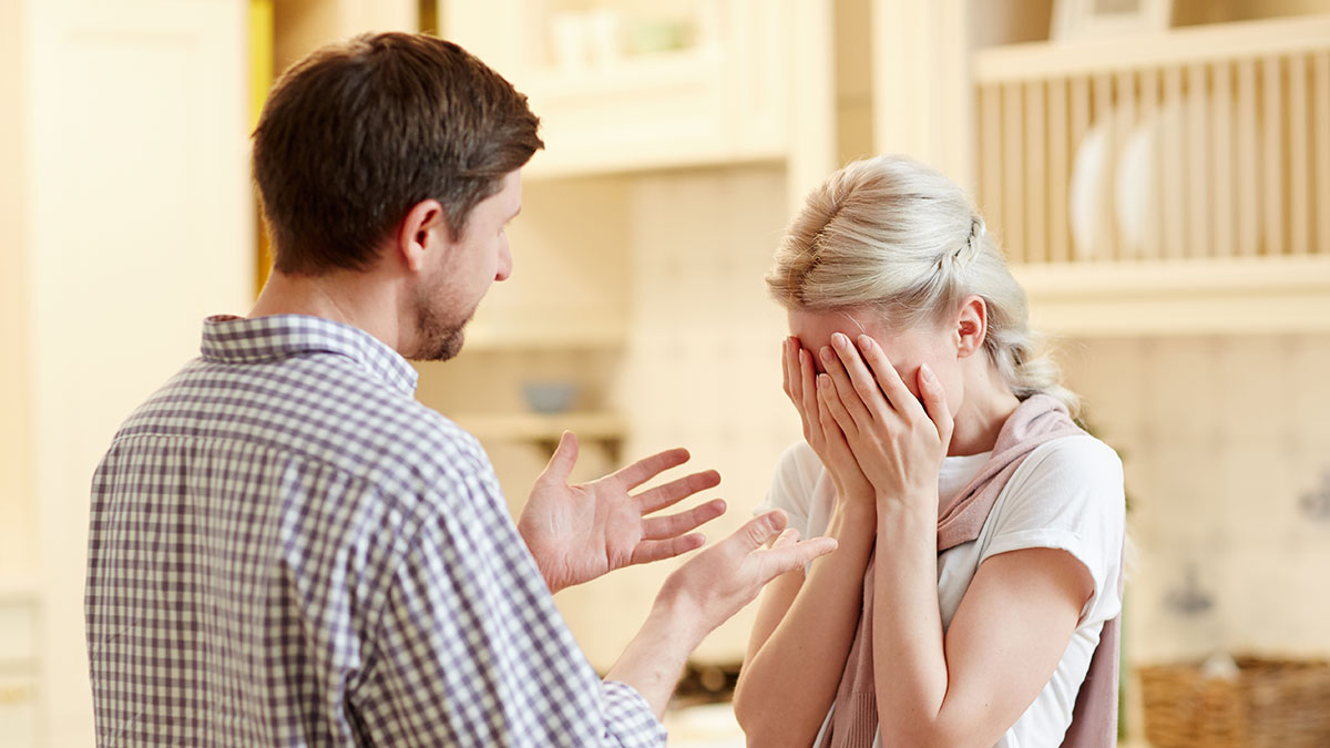 Woman covering face in distress as manipulative husband talks in kitchen, depicting emotional struggle and internet empowerment.