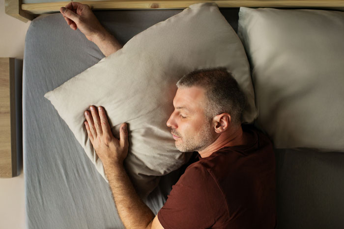 Man sleeping past noon in bed with pillow, highlighting parents wanting to wake him despite having pregnant wife at home. Man sleeping past noon in bed with pillow, highlighting parents wanting to wake him despite having pregnant wife at home.