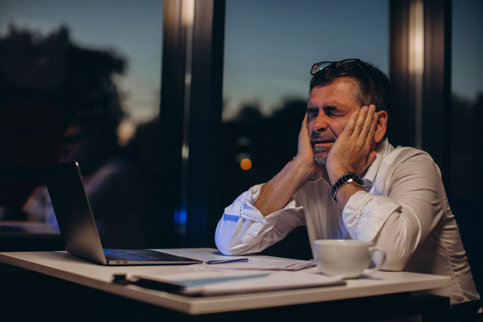 Man frustrated and tired at laptop late at night, reflecting stress from parents wanting to wake him despite pregnant wife. Man frustrated and tired at laptop late at night, reflecting stress from parents wanting to wake him despite pregnant wife.