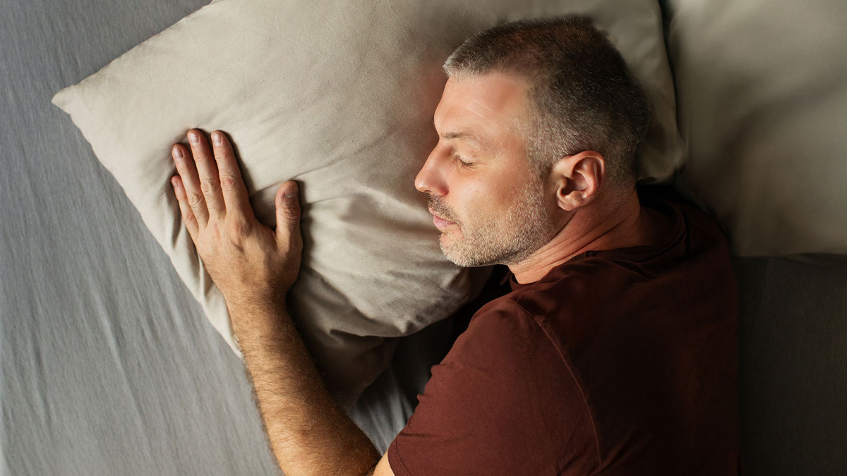 Man sleeping past noon on bed with pillow while parents want to wake him despite having pregnant wife nearby
