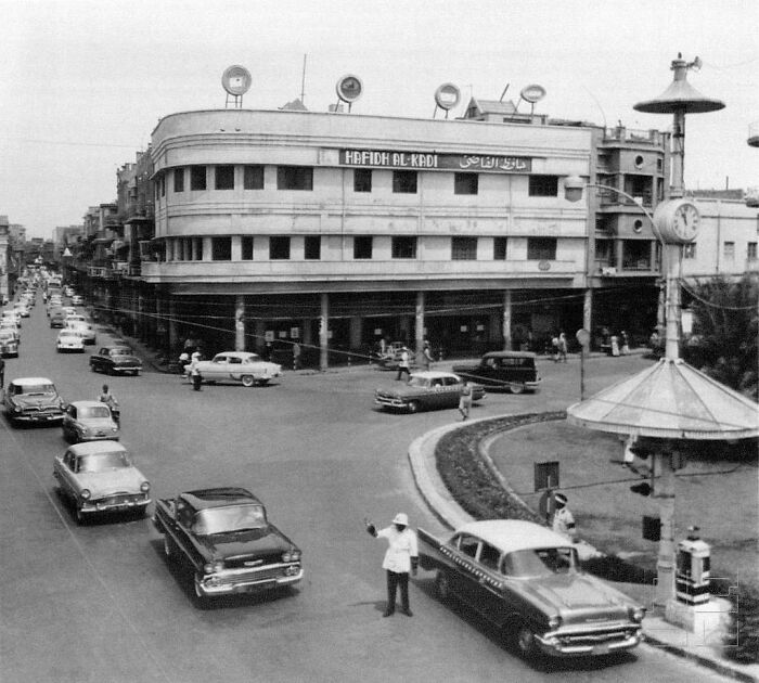 Vintage 1950s daily life photo showing busy street intersection with classic cars and people directing traffic globally.