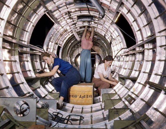 Women at work during WWII assembling aircraft parts inside a metal fuselage structure in a factory setting