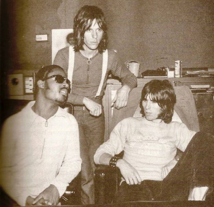 Three 1970s rock legends in a casual studio setting, collaborating and creating iconic music together.