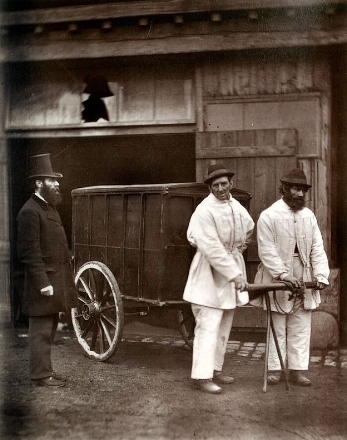 Victorian London poor workers in 1800s, two men pulling cart, one man standing nearby in historic urban setting.