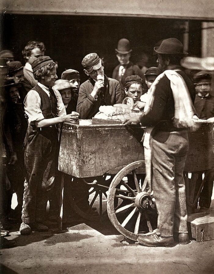 Group of London’s poorest buying food from street vendor by wooden cart in 1800s, showing how they really lived.