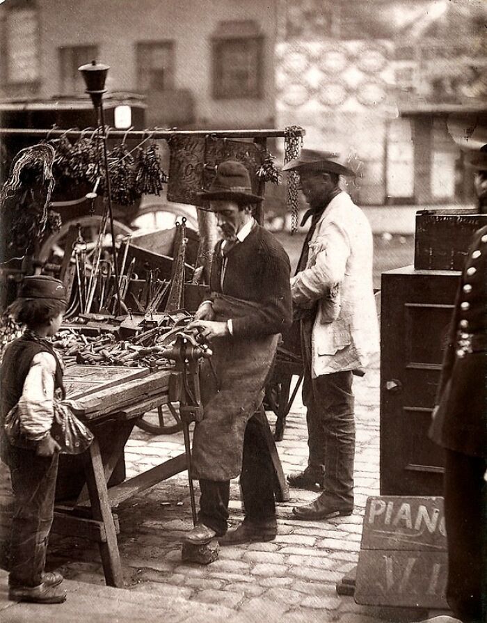 Street scene with London’s poorest men working and selling tools in a 1800s cobblestone market setting.