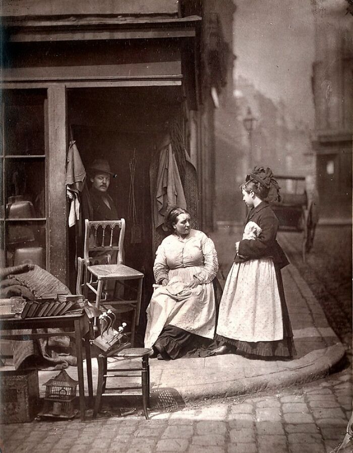 Victorian-era women and a man outside a London shop, depicting how London’s poorest really lived in the 1800s.