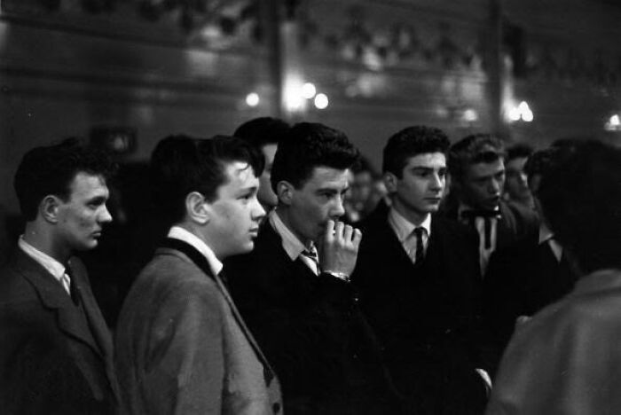 Group of young men in classic 20th century Teddy Boy era style suits at a social gathering, black and white photo.