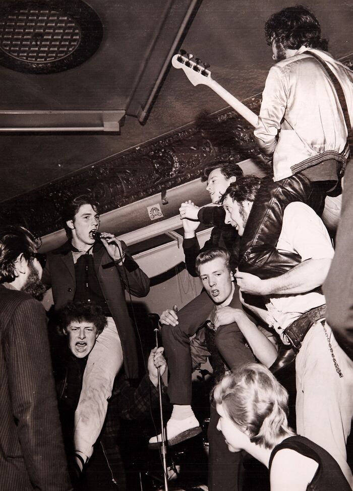 Teddy boy era band performing energetically with crowd interaction in a lively 20th century music venue.