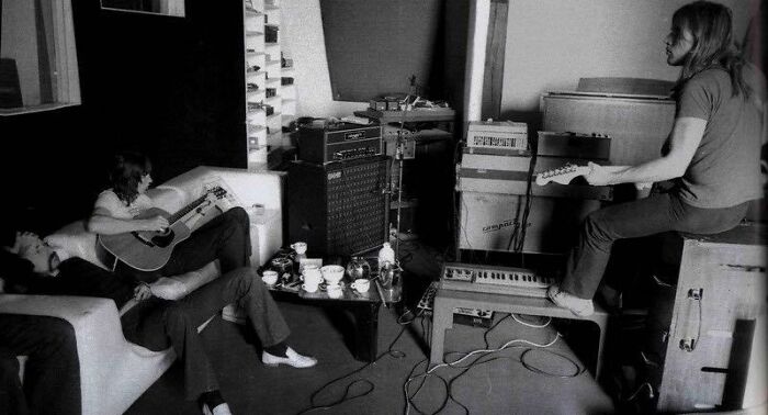 1970s rock legends creating music in a vintage studio with guitars, amplifiers, and recording equipment in a relaxed setting.