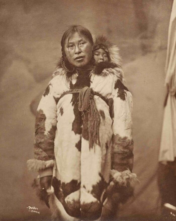 Historic photo of an Inuit woman wearing traditional fur clothing with a child on her back, capturing Inuit spirit and resilience.