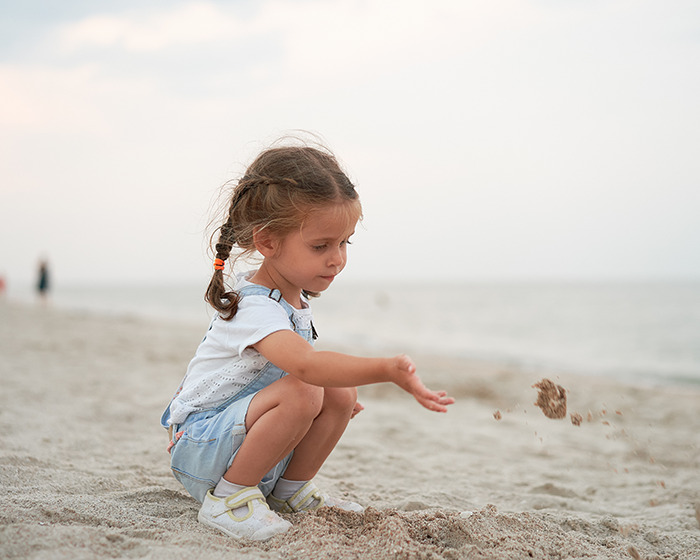 Young girl playing with sand on the beach during staged momfluencer pretend life photo session for online fame. Young girl playing with sand on the beach during staged momfluencer pretend life photo session for online fame.