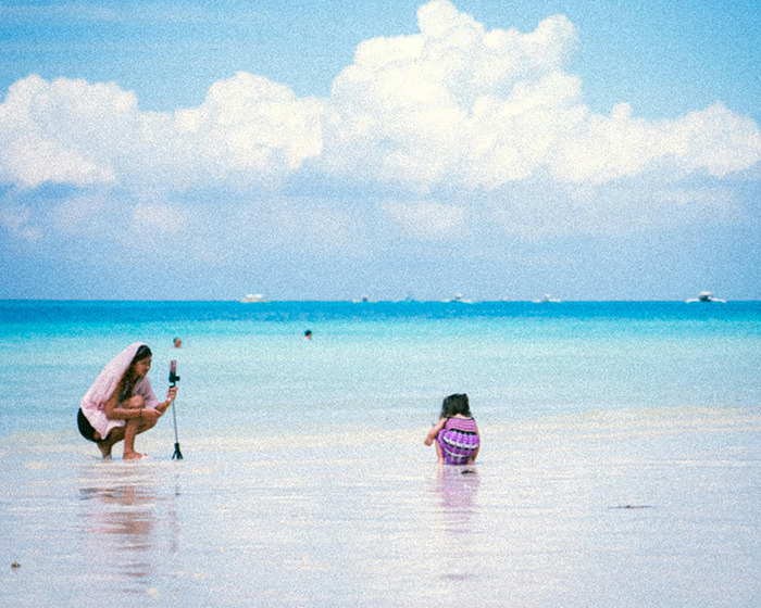 Momfluencer staging a beach day with daughter for online fame, capturing photos by the ocean under blue sky. Momfluencer staging a beach day with daughter for online fame, capturing photos by the ocean under blue sky.