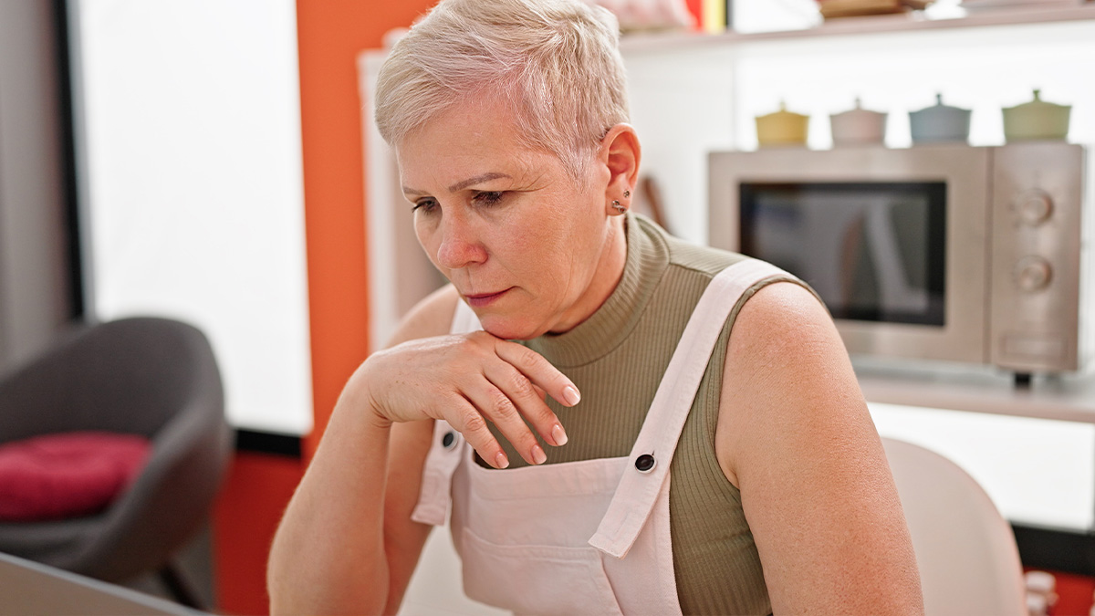 Middle-aged woman looking concerned at a laptop, reflecting family drama over inherited house with aunt living rent-free.
