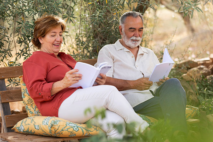 Older couple sitting on a bench outdoors, reading documents and discussing genetic heritage information with smiles. Older couple sitting on a bench outdoors, reading documents and discussing genetic heritage information with smiles.