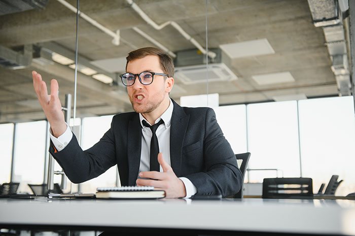 Professional man in a black suit and glasses gesturing passionately during a job interview in a modern office setting. Professional man in a black suit and glasses gesturing passionately during a job interview in a modern office setting.
