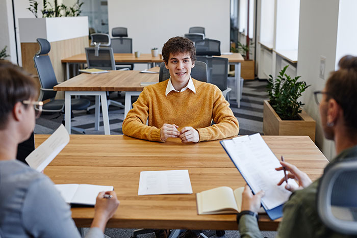 Young man in a mustard sweater attending a job interview with a high chance of getting hired, sitting at a conference table. Young man in a mustard sweater attending a job interview with a high chance of getting hired, sitting at a conference table.