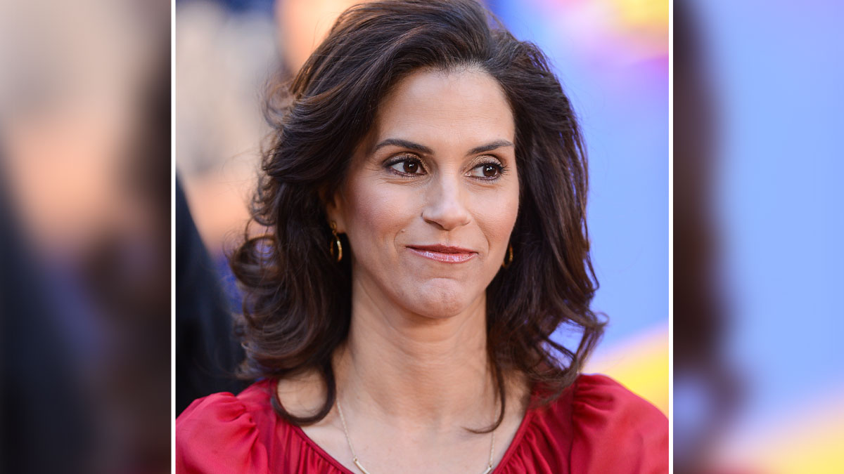 Jami Gertz attending a public event, wearing a red outfit with natural makeup and styled dark hair.