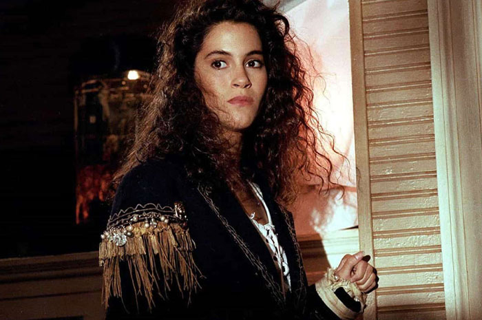 Jami Gertz with voluminous curly hair wearing a black jacket with fringe and bead details in an indoor setting. Jami Gertz with voluminous curly hair wearing a black jacket with fringe and bead details in an indoor setting.
