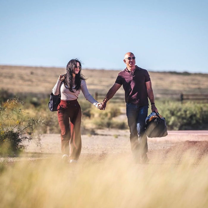 Jeff Bezos walking hand in hand with Lauren Sánchez in a desert setting, showing his changed hair look. Jeff Bezos walking hand in hand with Lauren Sánchez in a desert setting, showing his changed hair look.