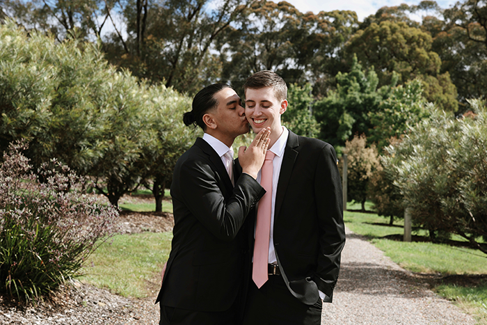 Gay couple dressed in suits sharing a tender moment outdoors in a park with trees and greenery around. Gay couple dressed in suits sharing a tender moment outdoors in a park with trees and greenery around.