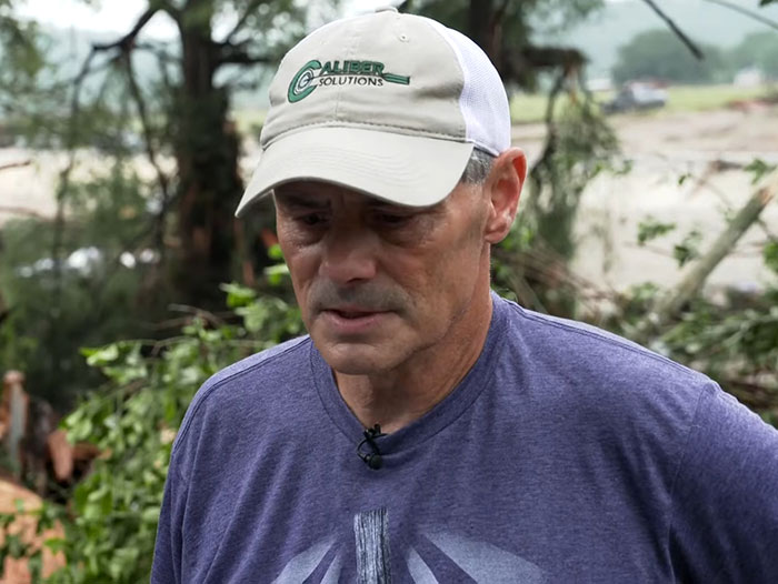 Man wearing a Capiber Solutions hat looks concerned, standing outdoors near flood-damaged area reflecting flood victim fear. Man wearing a Capiber Solutions hat looks concerned, standing outdoors near flood-damaged area reflecting flood victim fear.