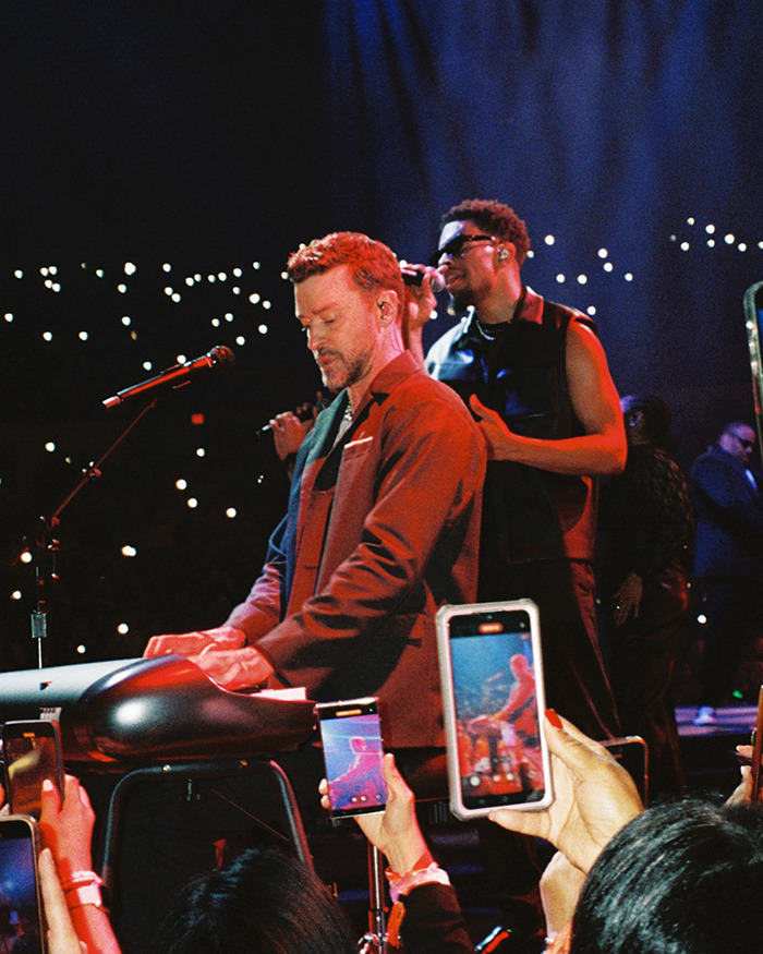 Justin Timberlake performing on stage with band, amid crowd capturing the concert on smartphones. Justin Timberlake performing on stage with band, amid crowd capturing the concert on smartphones.
