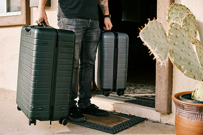 Man holding two suitcases outside house, symbolizing upgrade to flirty bachelor after public demotion by girlfriend. Man holding two suitcases outside house, symbolizing upgrade to flirty bachelor after public demotion by girlfriend.