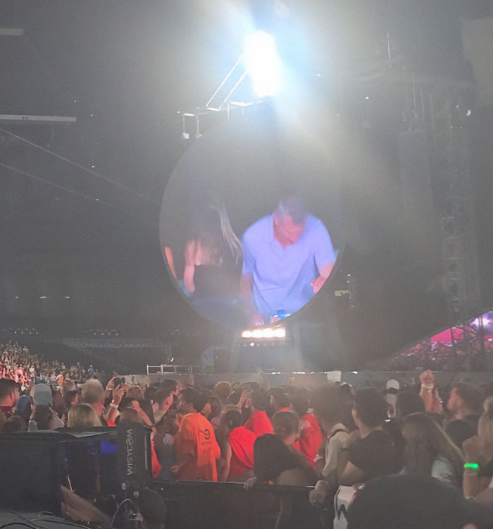 Crowd at Coldplay concert with large round screen showing performer amid bright stage lights and security staff. Crowd at Coldplay concert with large round screen showing performer amid bright stage lights and security staff.