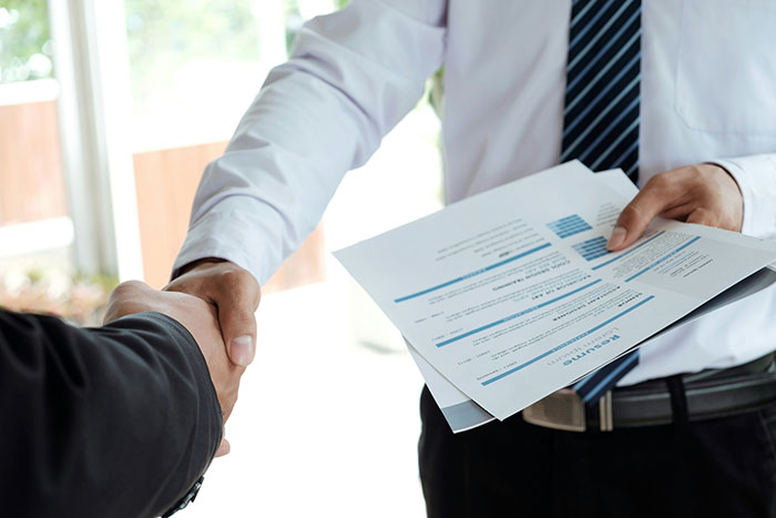 Person gets laid off shaking hands while holding resumes, symbolizing landing a better job through perseverance. Person gets laid off shaking hands while holding resumes, symbolizing landing a better job through perseverance.