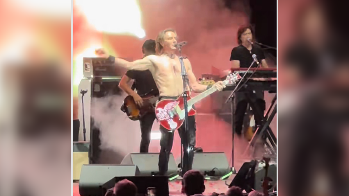 75-year-old rockstar performing shirtless on stage with guitar, backed by band members and colorful stage lights and smoke.