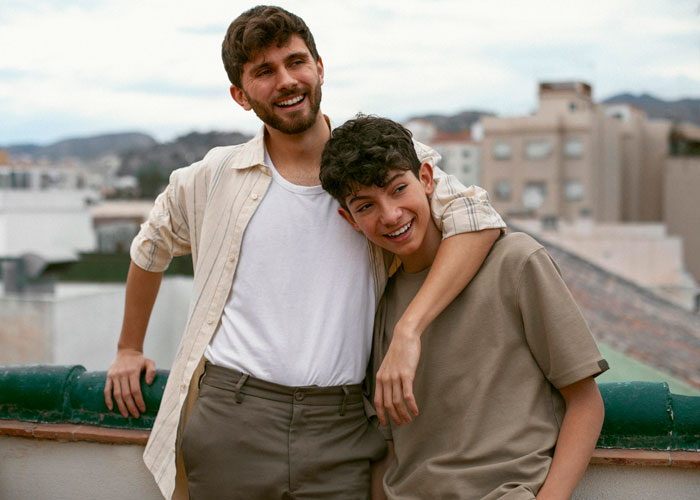 Two brothers on a rooftop, smiling and embracing, representing a teen working two jobs to survive after losing parents. Two brothers on a rooftop, smiling and embracing, representing a teen working two jobs to survive after losing parents.