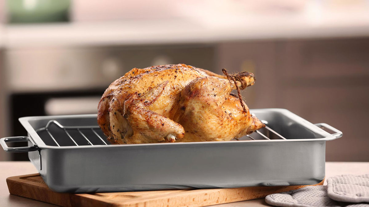 Roasted whole chicken in a metal pan on a kitchen counter highlighting raw chicken biohazard concerns.