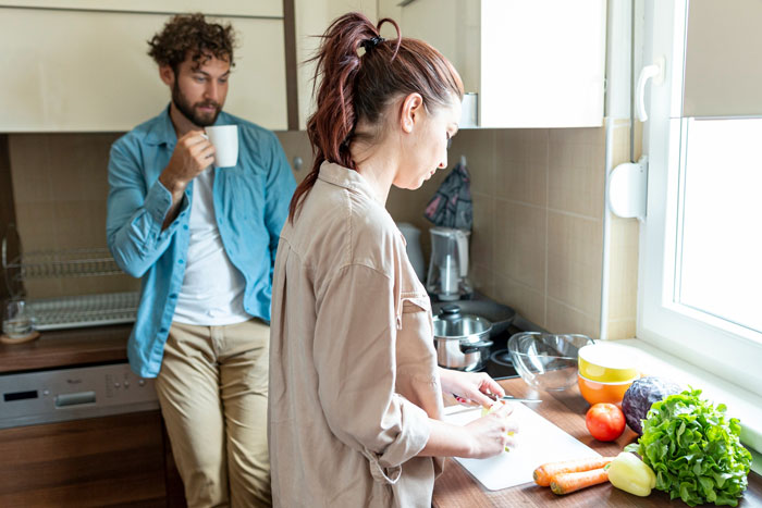 Husband drinking coffee watching wife prepare food in kitchen after raw chicken biohazard incident in trunk. Husband drinking coffee watching wife prepare food in kitchen after raw chicken biohazard incident in trunk.