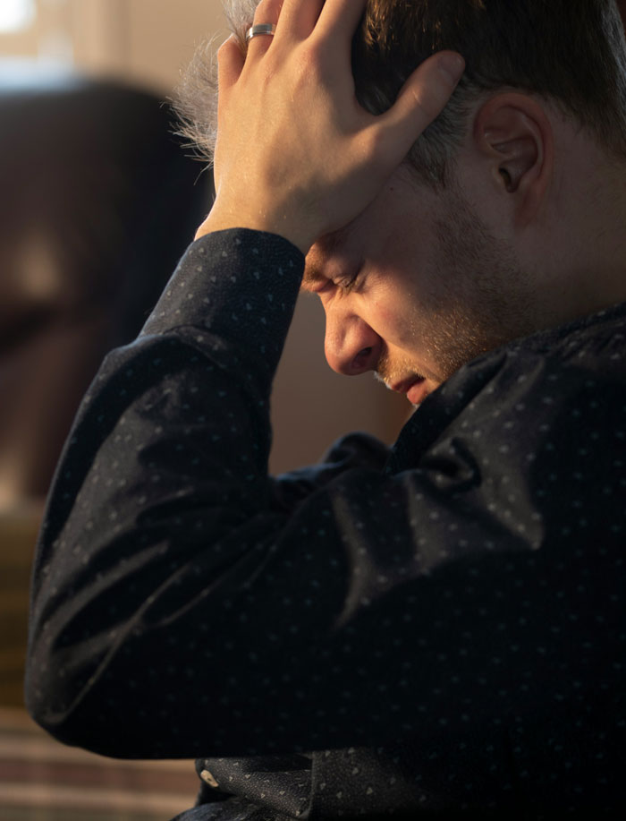 Man holding head in frustration indoors, showing emotions linked to reading wife’s diary behind her back. Man holding head in frustration indoors, showing emotions linked to reading wife’s diary behind her back.