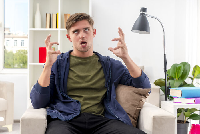 Frustrated man sitting on couch gesturing in a modern living room, reflecting emotions of a guy fed up with pregnant roomie.