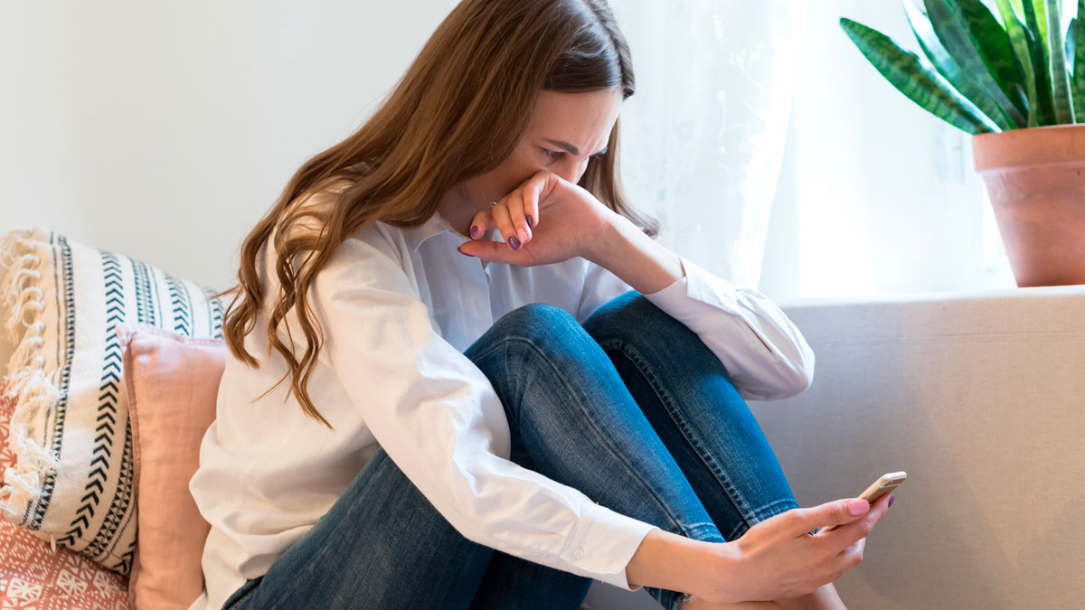 Young woman looking distressed over phone, reflecting on a man failing social media story test and moving on.