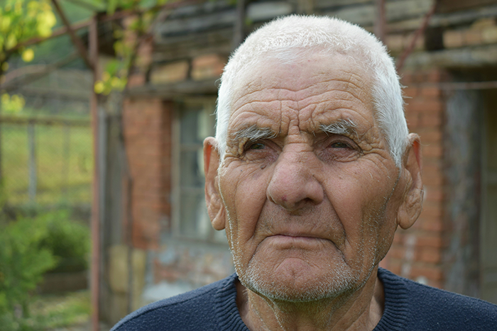 Elderly quiet retiree standing outdoors near a brick building, reflecting a surprising neighborhood story.