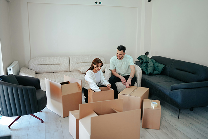Young couple surrounded by moving boxes in living room, symbolizing man’s upgrade to flirty bachelor after friendship demotion. Young couple surrounded by moving boxes in living room, symbolizing man’s upgrade to flirty bachelor after friendship demotion.