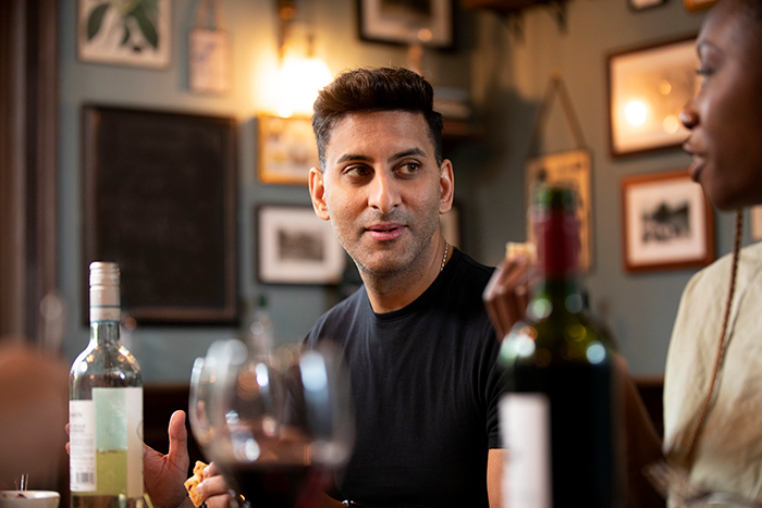 Man in black shirt confidently socializing at a bar, embodying flirty bachelor vibes after public demotion by girlfriend. Man in black shirt confidently socializing at a bar, embodying flirty bachelor vibes after public demotion by girlfriend.