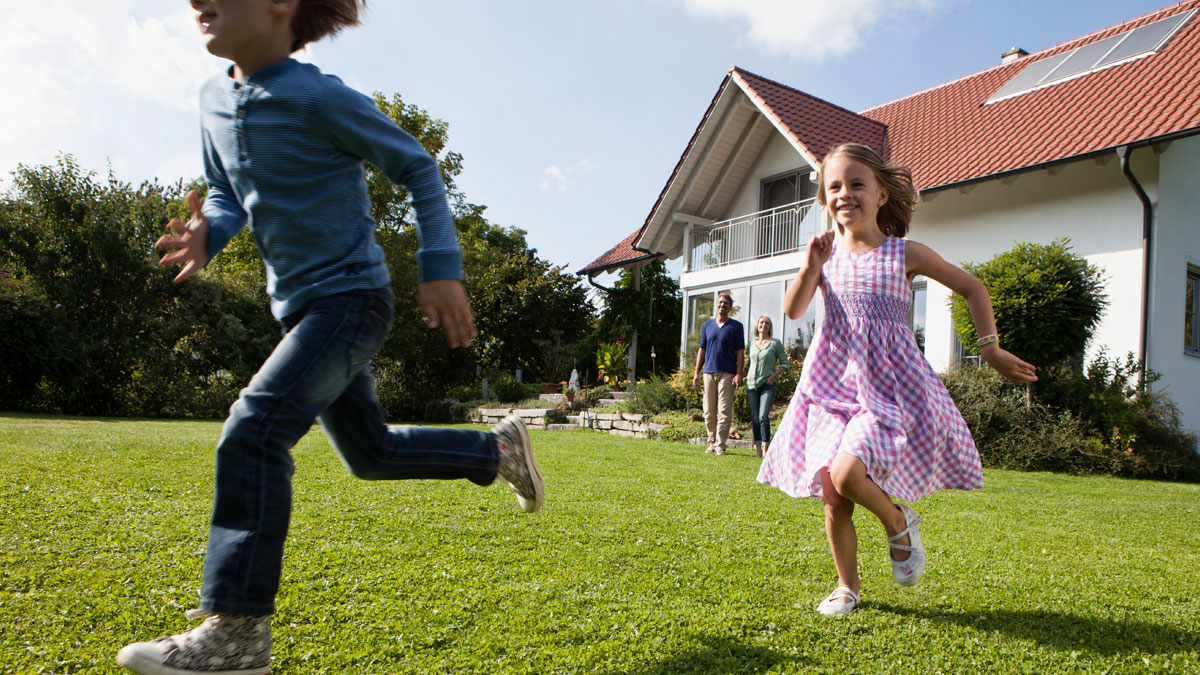 Children running on green lawn outside house with parents in background, illustrating man banning children from property.