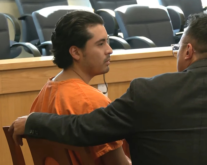 Man wearing orange prison uniform in court with lawyer discussing case related to slaying entire family and dog. Man wearing orange prison uniform in court with lawyer discussing case related to slaying entire family and dog.