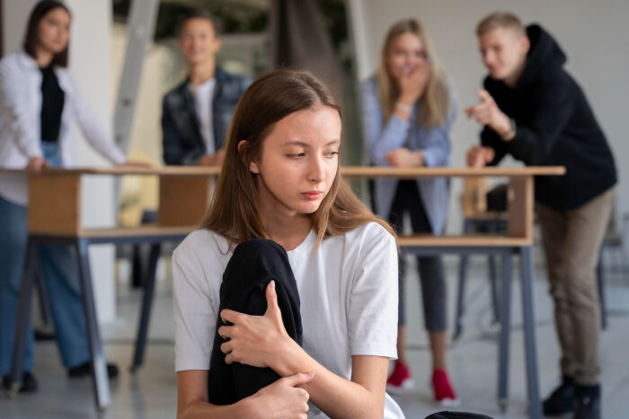 Teen girl feeling isolated while other kids gossip in the background, highlighting manipulation advice given to kids.