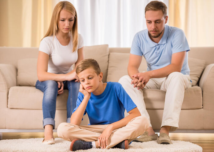 A sad boy sitting on the floor with concerned parents behind him, reflecting on advice and manipulation.