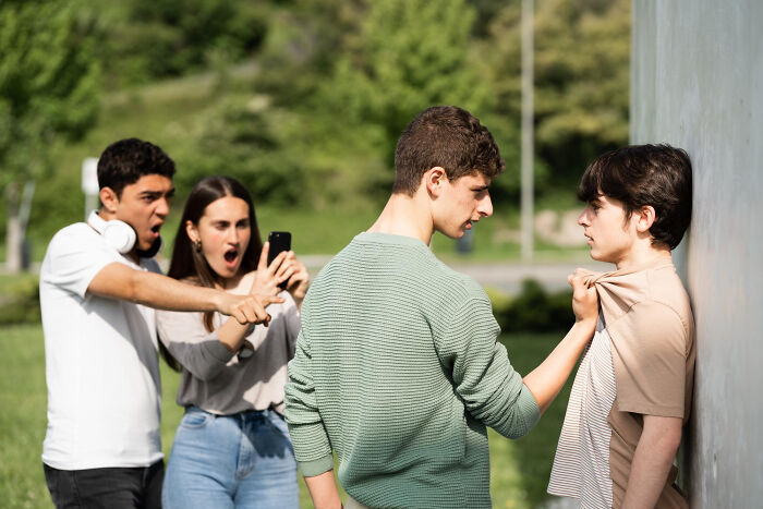 Teen boy bullying another against a wall while friends record and point, illustrating manipulation in advice kids were given.
