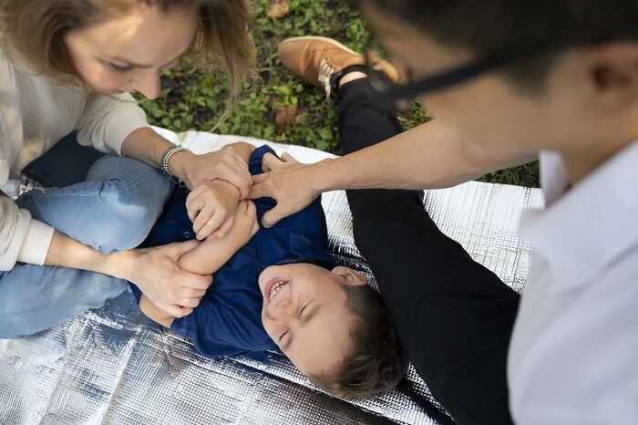 Parents playfully tickling child outdoors, illustrating kids advice and subtle manipulation in family interactions.
