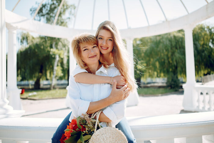 Mother and teenage daughter smiling outdoors, embracing under a white pergola, illustrating advice kids were given.