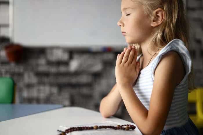 Young girl praying with closed eyes at a table, reflecting on advice kids were given that was manipulation in disguise